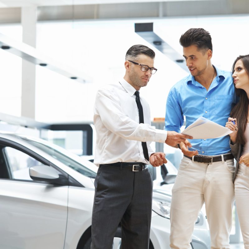 Young Couple Signing a Contract in Car Showroom.